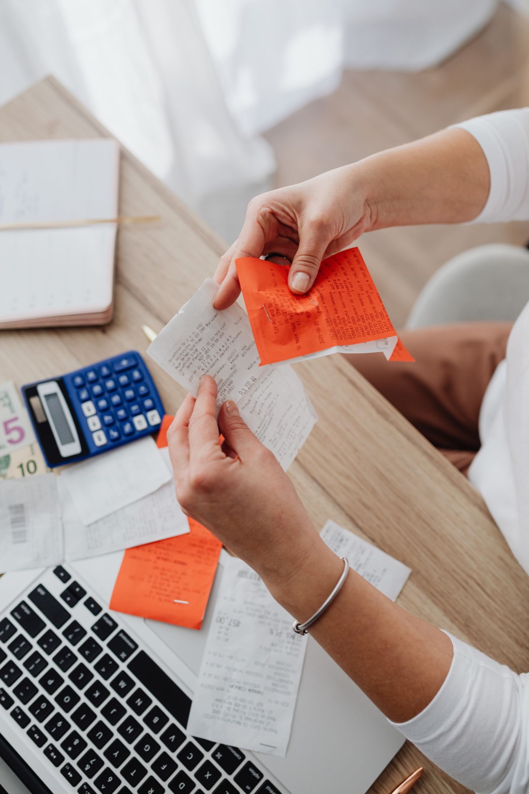Hands sorting through receipts next to a calculator and laptop